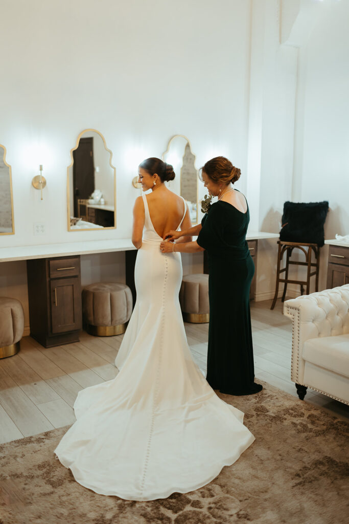 Mother helping the bride button up her gown