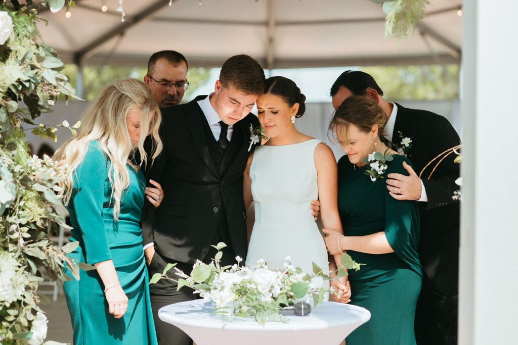 Family gather around the bride and groom for an emotional moment at their brick and mortar wedding ceremony