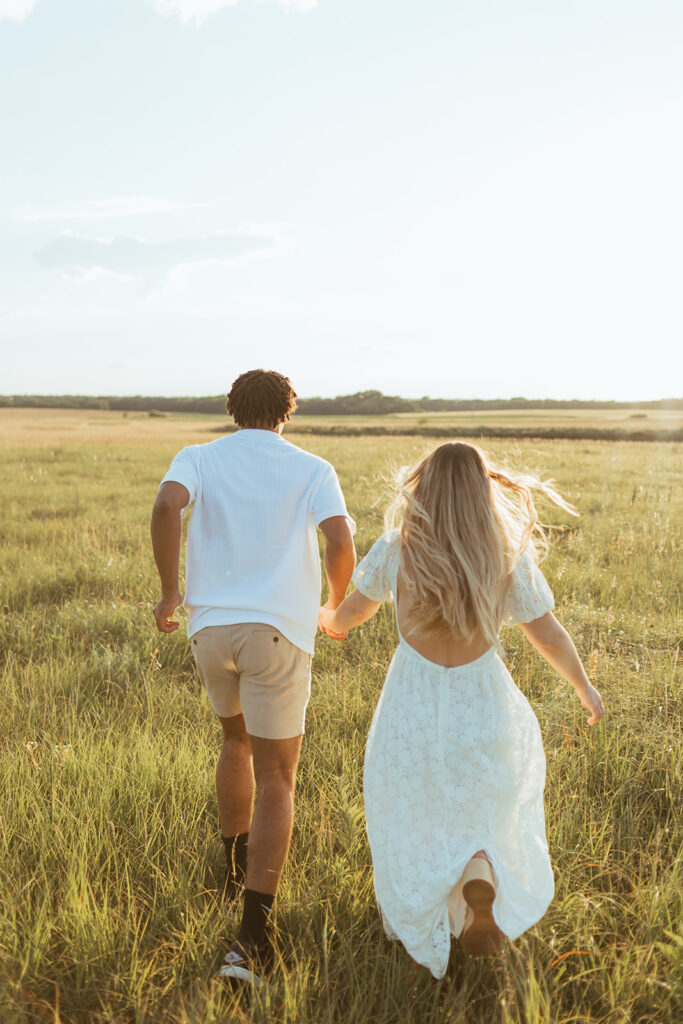 A couple frolics through a grassy field during their summer engagement photos