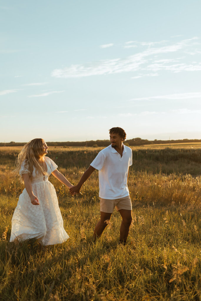 A couple frolics through a field in Kansas during their engagement session at Sunset