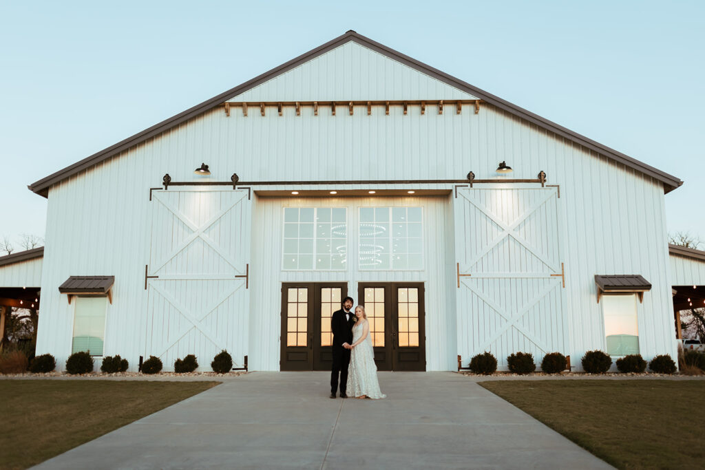 Bride and groom stand in front of a white barn Wichita wedding venue