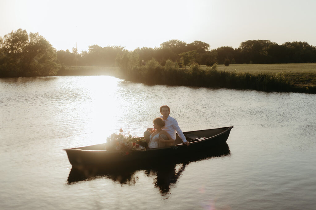 Bride and groom sit in a canoe with romantic florals in the pond at Atreeum greenhouse venue